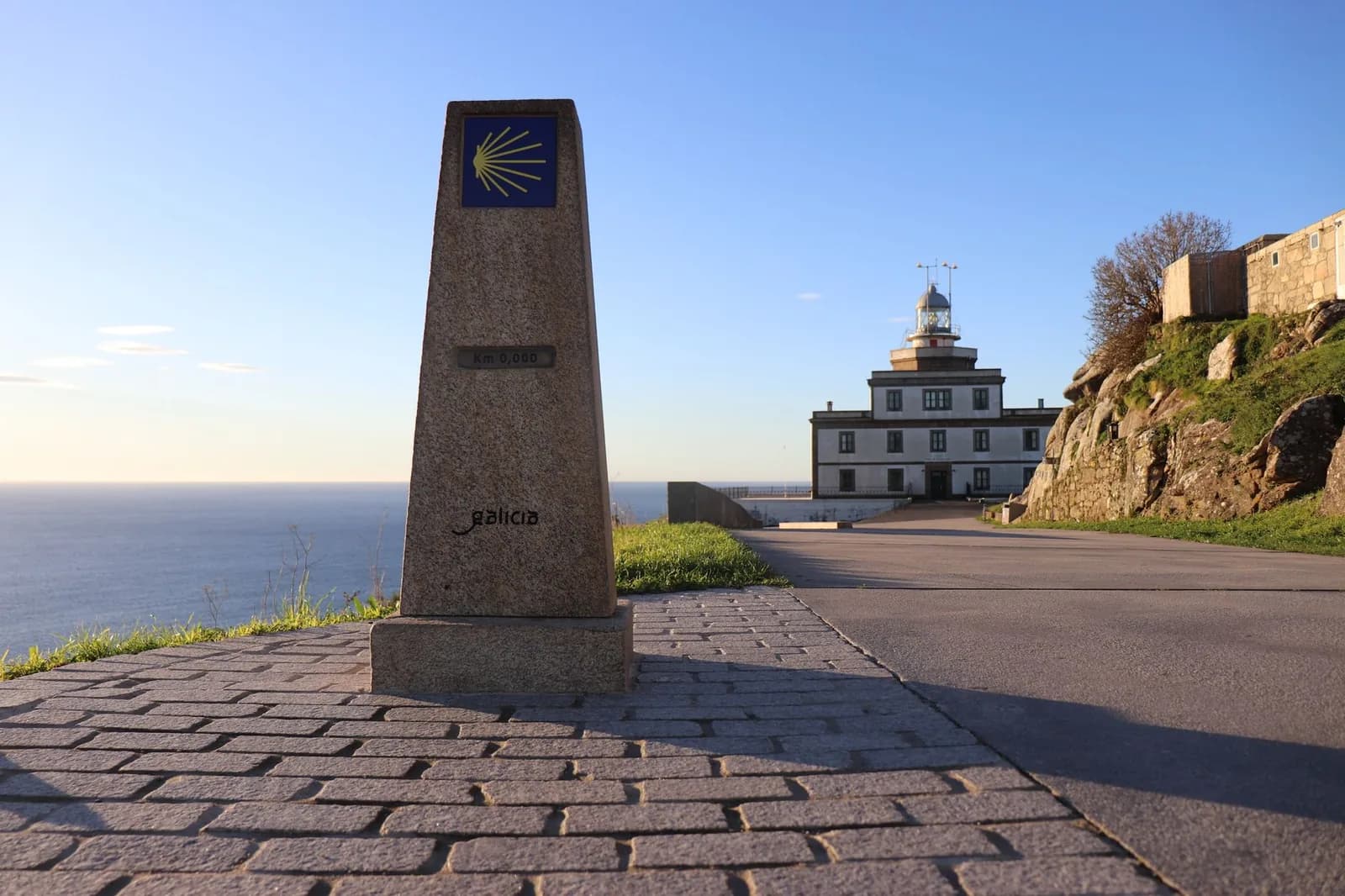 La borne du kilomètre zéro du Camino, marquée de la coquille jaune, devant le phare de Fisterra en Galice