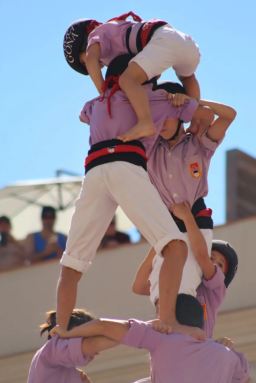 Des castellers en chemise rose montant une tour humaine, les enfants casqués au sommet