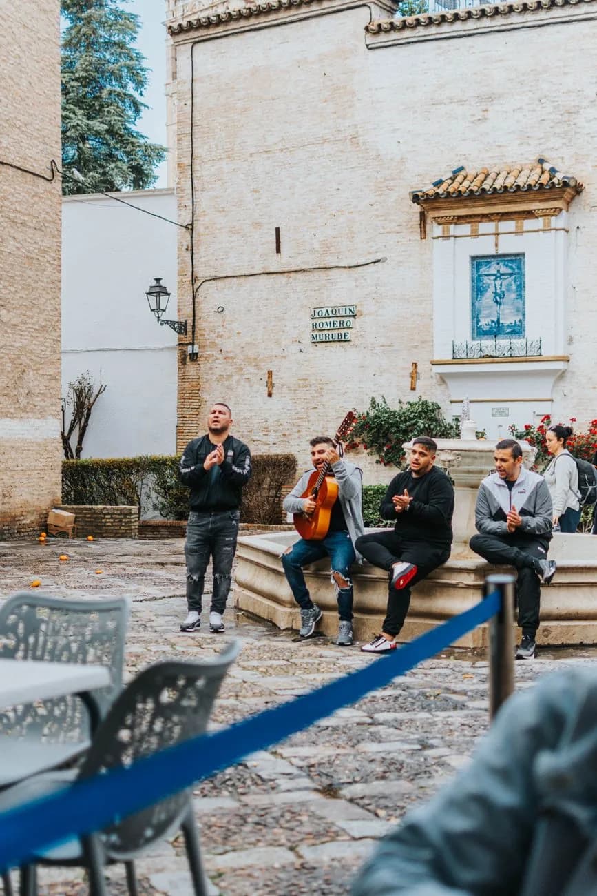 Quatre hommes chantant, jouant de la guitare et frappant des palmas autour d'une fontaine dans une place de Séville