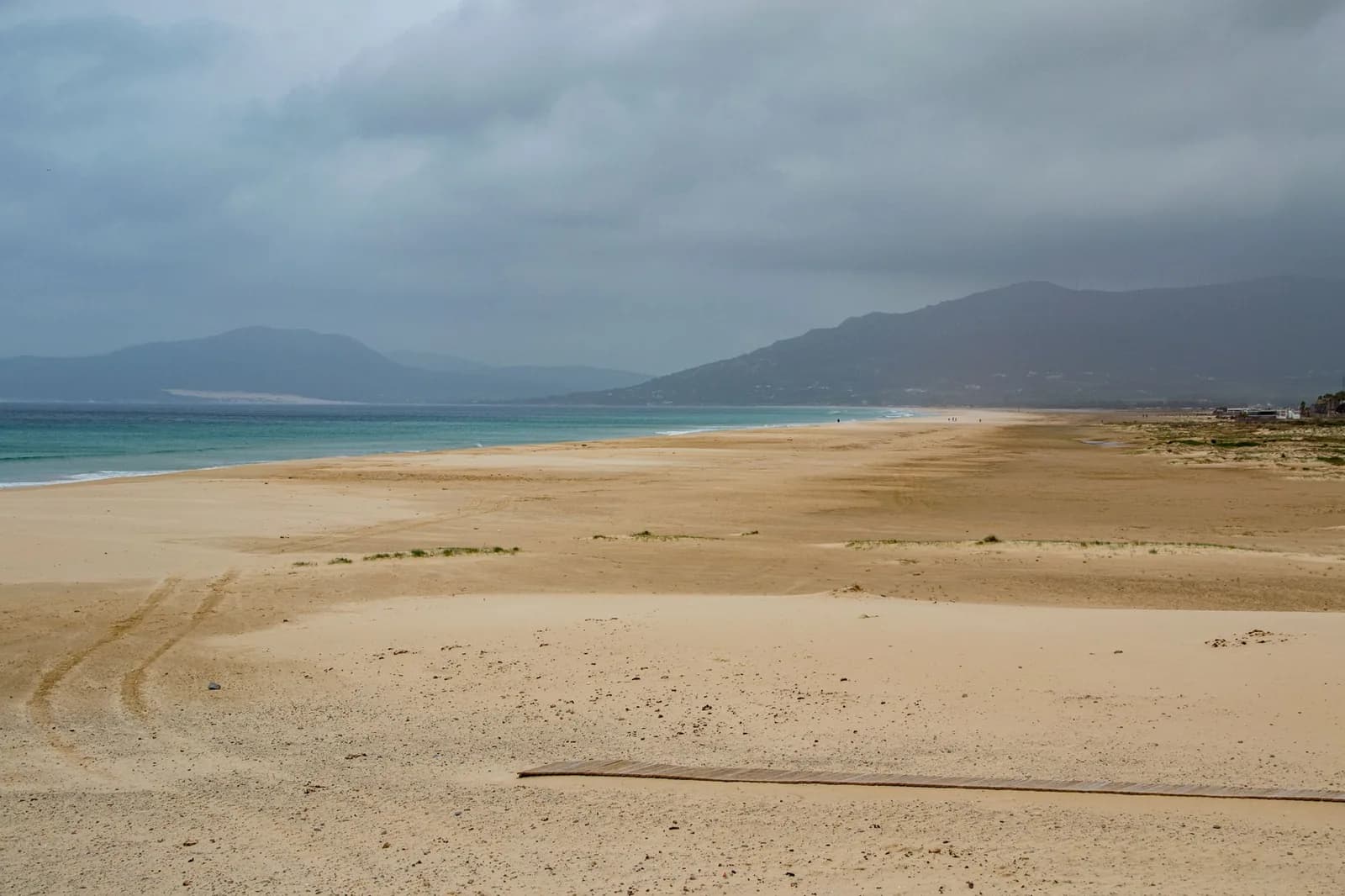 Une immense plage de sable déserte sur la côte atlantique andalouse, sous un ciel gris et devant des collines