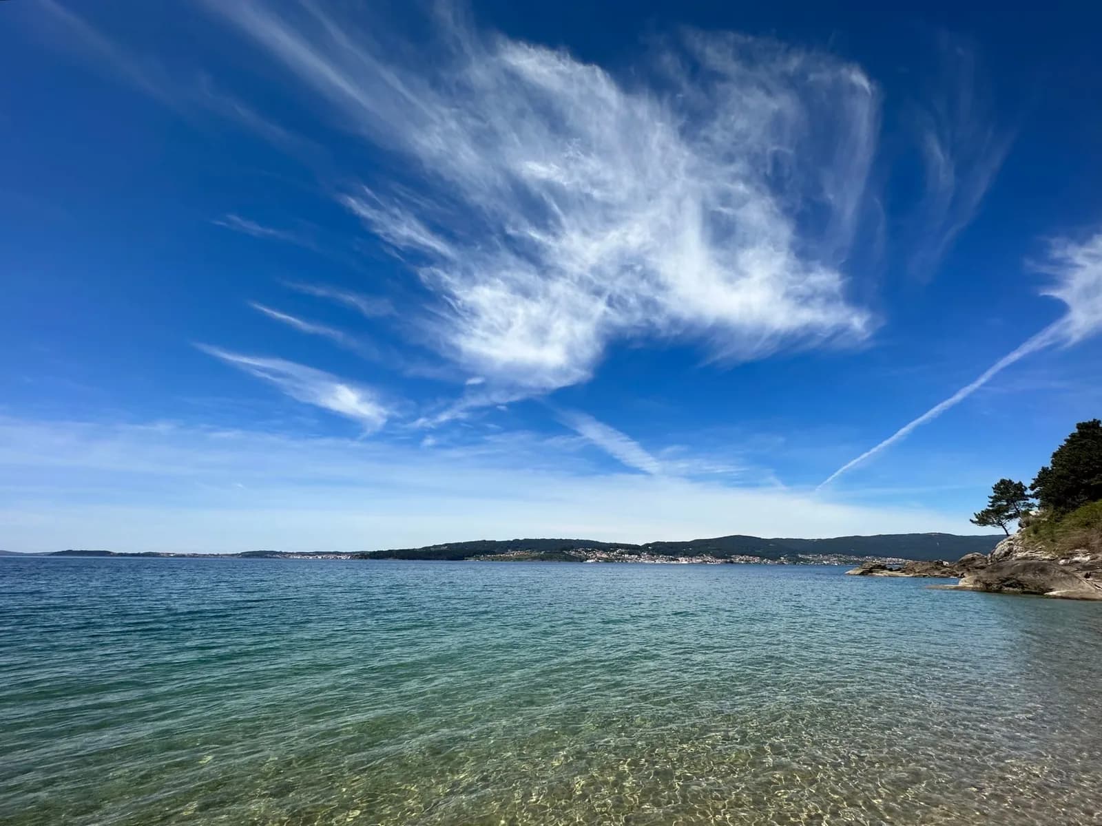 Une plage de ría en Galice, son eau transparente et la rive boisée d'en face
