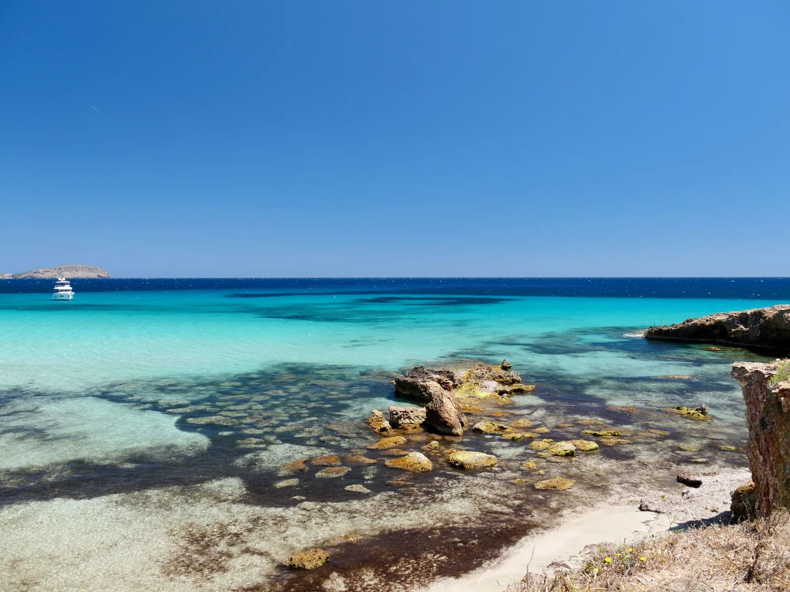 Une crique d'Ibiza aux eaux turquoise et peu profondes, un îlot à l'horizon