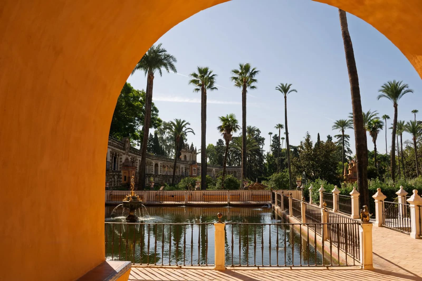 Les jardins du Real Alcázar de Séville vus sous une arche ocre, le bassin de Mercure et la galerie du Grutesco