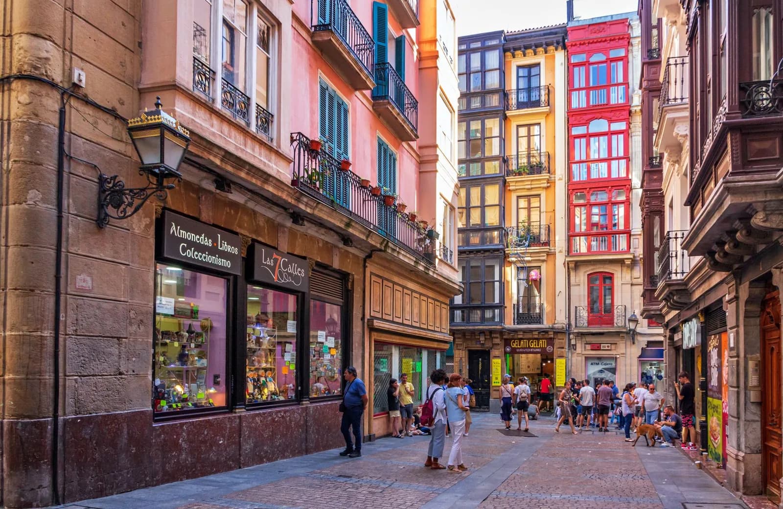 Une rue piétonne du Casco Viejo de Bilbao, ses miradores vitrés colorés et une enseigne portant le nom Las 7 Calles