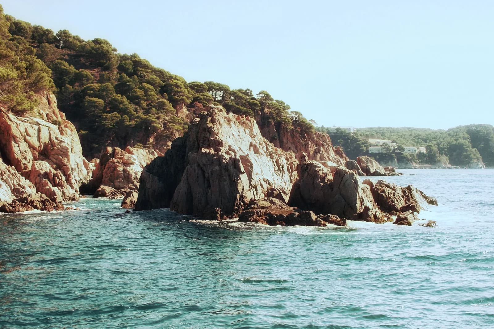 Une pointe rocheuse de la Costa Brava couverte de pins, plongeant dans une mer turquoise