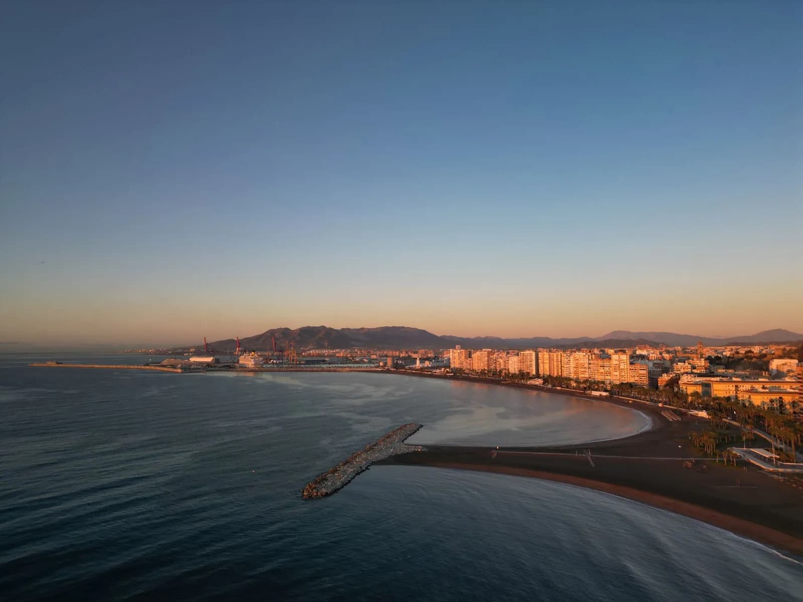 Vue aérienne des plages et de la baie de Málaga au coucher du soleil, avec le port, la ville et la sierra en arrière-plan