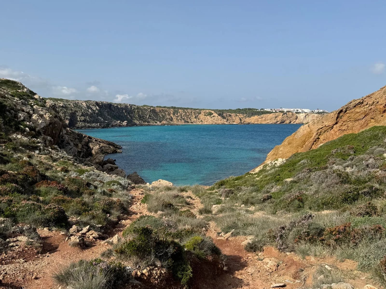 Sentier côtier descendant vers une crique turquoise sur la côte nord de Minorque, sur le tracé du Camí de Cavalls