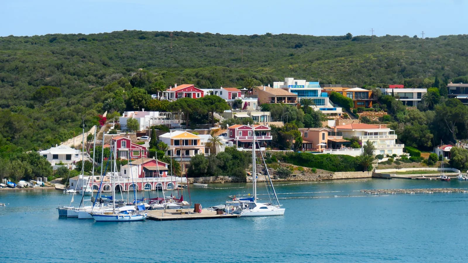 Voiliers amarrés dans la rade de Mahón à Minorque, maisons colorées sur la rive boisée