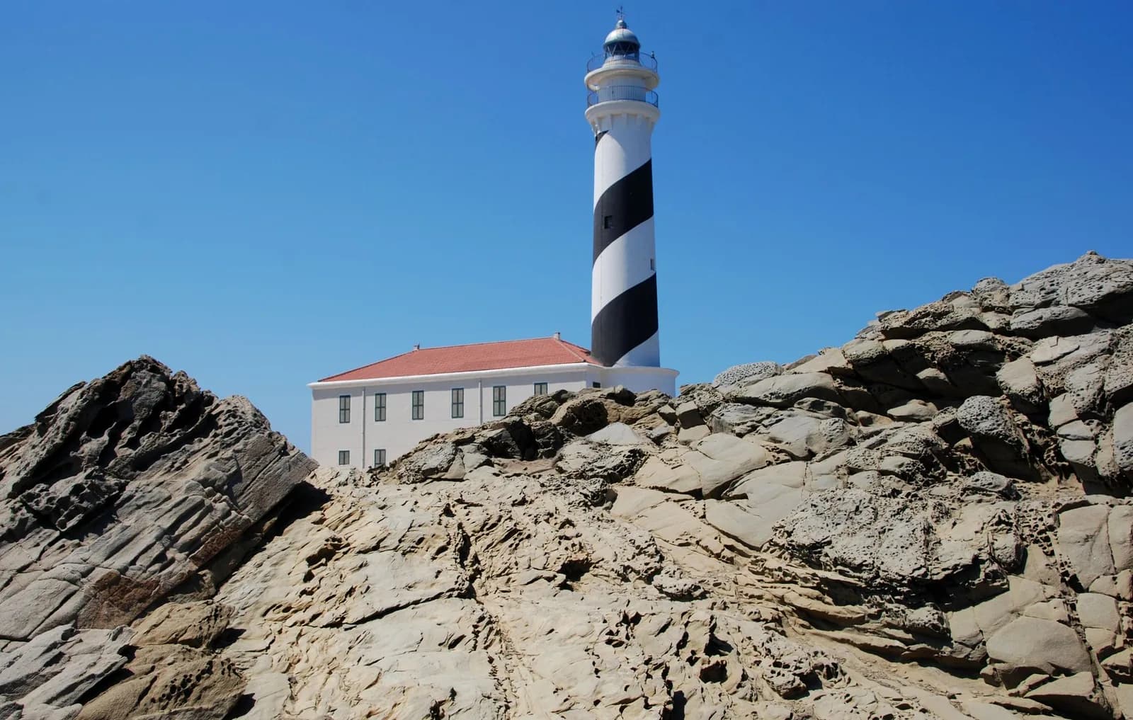 Phare rayé noir et blanc du cap de Favàritx sur un rocher d'ardoise, à Minorque