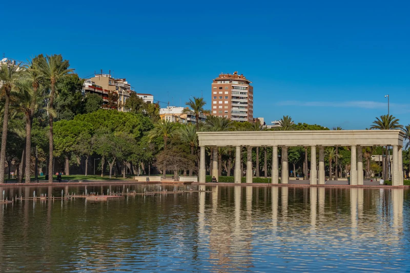 Le jardin du Turia à Valence, sa colonnade blanche réfléchie dans un bassin, palmiers et immeubles au-dessus de l'ancien lit du fleuve