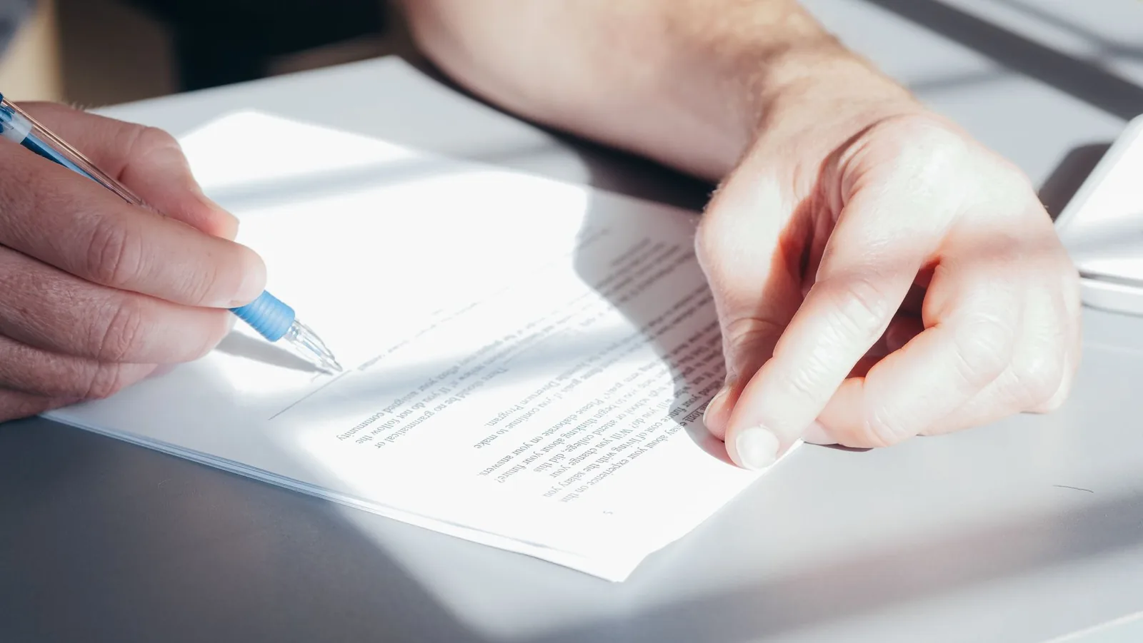 Une main remplit au stylo un formulaire administratif posé sur un bureau